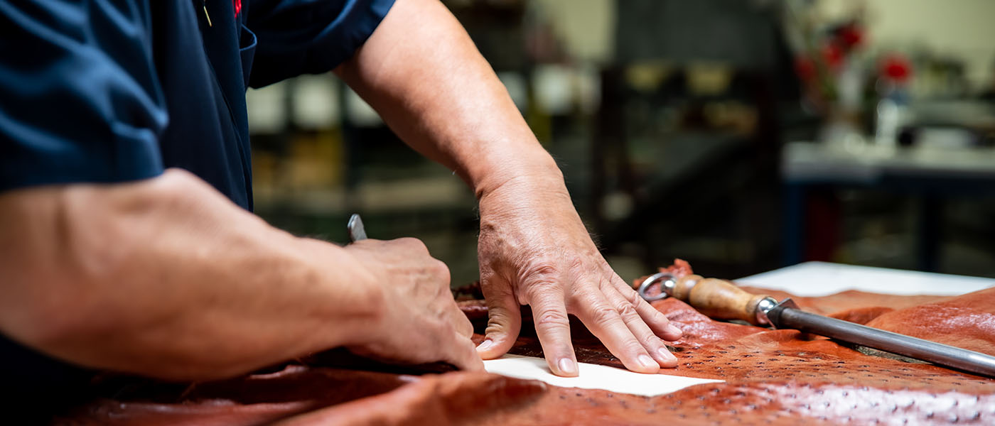 Man cuts exotic leather with knife.